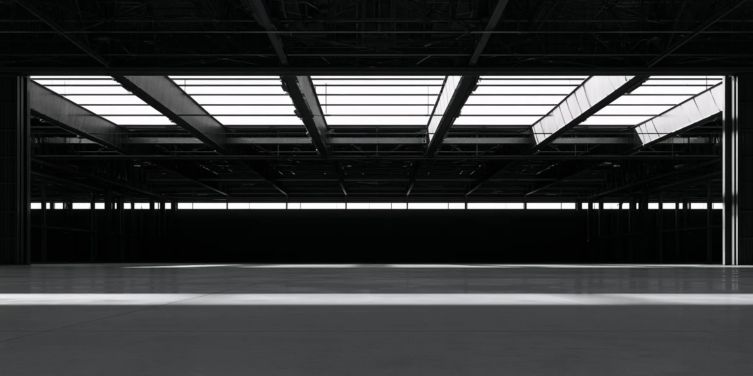 An empty hangar interior in silhouette, skylights glowing overhead